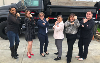 6 women by dump truck striking rosie the riveter pose